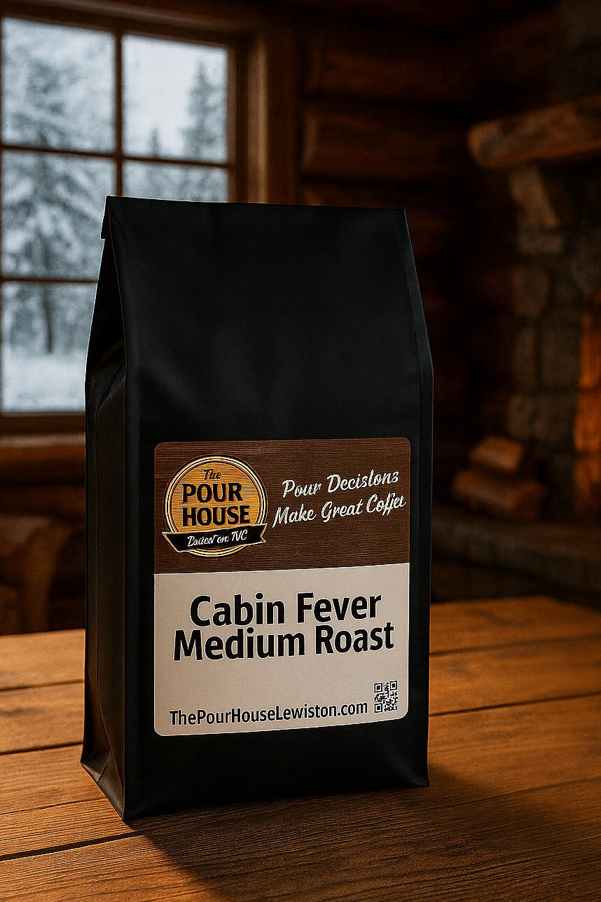 Bag of Cabin Fever Medium Roast coffee from The Pour House on a wooden surface with a fireplace in the background.